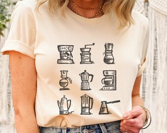 May include: A beige t-shirt with a graphic of nine different coffee makers in black and white. The coffee makers include a French press, a percolator, a drip coffee maker, and a pour-over coffee maker.