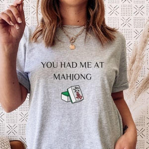 May include: Gray t-shirt with the text "You had me at Mahjong" and a graphic of mahjong tiles.