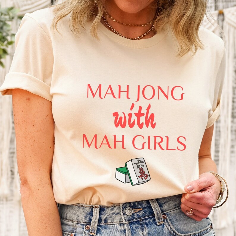 May include: A cream colored t-shirt with the text "Mah Jong with Mah Girls" in red. The shirt features a green and white mah jong tile.