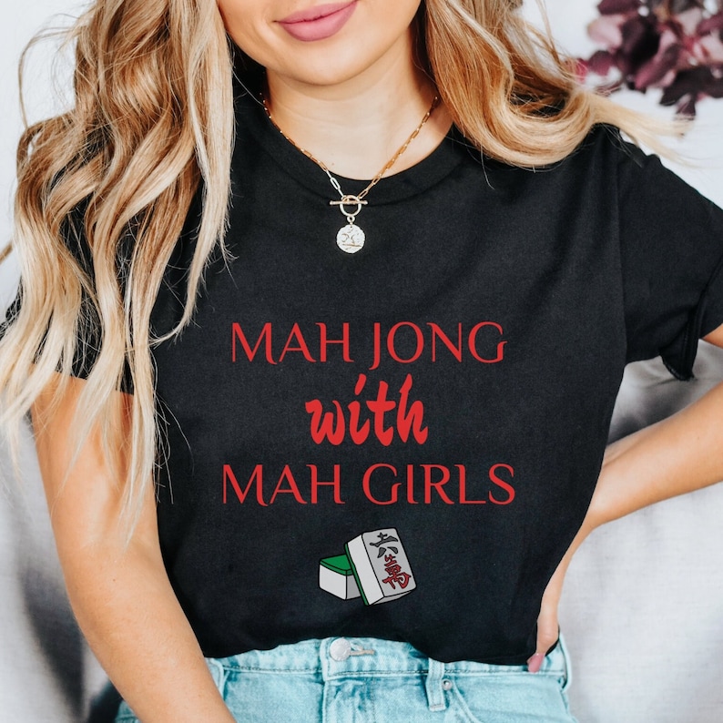 May include: Black t-shirt with the text "Mahjong with Mah Girls" in red lettering. A green and white mahjong tile is pictured below the text.