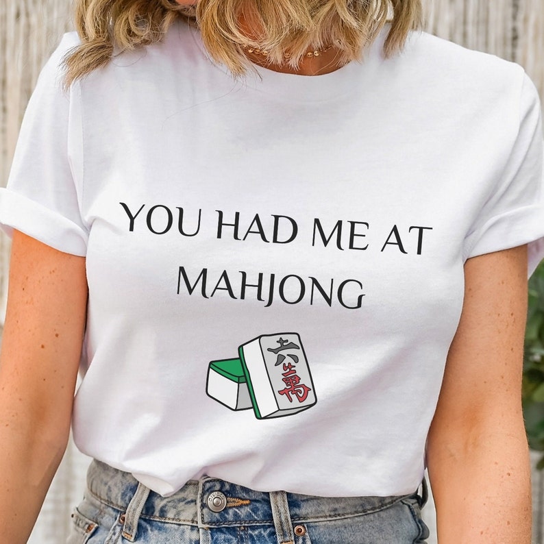 May include: White t-shirt with the text "YOU HAD ME AT MAH JONG" and a graphic of two mahjong tiles.
