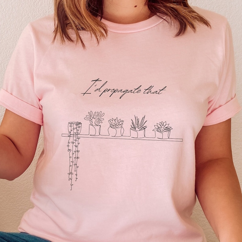 May include: A pink t-shirt with the text "I'd propagate that" and a line drawing of potted plants on a shelf.