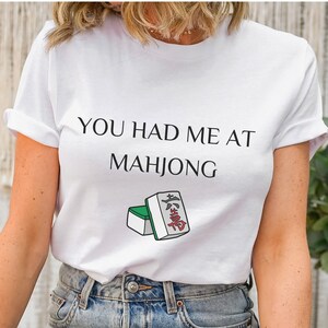 May include: White t-shirt with the text "You had me at Mahjong" and a green and white mahjong tile with red Chinese characters.