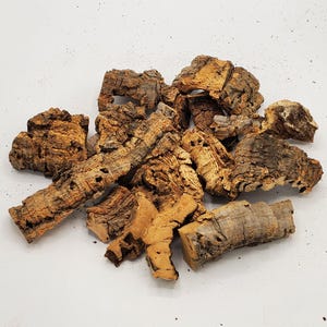 Puede incluir: Un montón de trozos de corteza de corcho marrón, algunos con una textura rugosa y otros con una superficie más lisa. La corteza es un material natural y tiene una variedad de formas y tamaños.