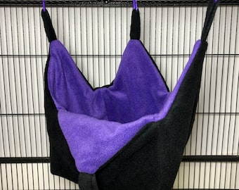 May include: Purple and black hanging hammock for small pets, made of soft fleece fabric. It has two purple clips for hanging.