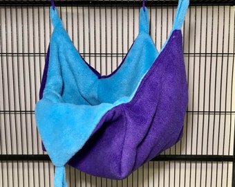 May include: A blue and purple hanging hammock for small pets, made of soft fleece fabric. It has two purple loops for hanging.
