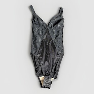 May include: A black bodysuit with a V-neckline and spaghetti straps. The bodice features a satin-like material with lace detailing on the upper chest and sides. The bottom portion has a hook and eye closure.