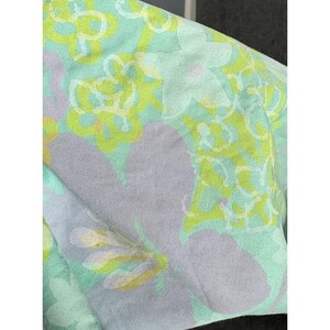 May include: Close-up of a fabric with a floral pattern. The design features large, light purple flowers and smaller, yellow and white flowers on a light green background. The fabric appears soft and slightly creased.