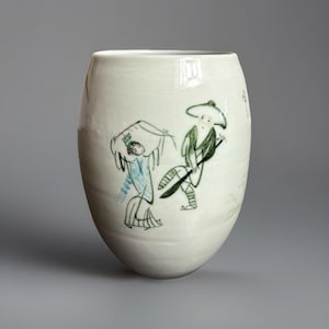 Könnte beinhalten: Weiße Keramikvase mit handbemaltem Design aus zwei Figuren in Grün, Blau und Weiß. Die Figuren tragen Hüte und scheinen zu tanzen.