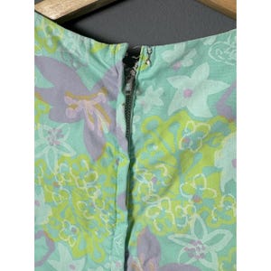 May include: Close-up of a vintage dress neckline with a floral pattern. The dress has a zip closure and features a repeating pattern of flowers in shades of green, lavender, and white on a light turquoise background.