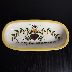 May include: Oval ceramic serving dish with a yellow rim and a white interior. The dish is decorated with a floral design and the text "For celery, olives, pickles, and such like."