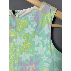 May include: A sleeveless dress with a floral pattern. The dress has a light blue background with white, yellow, and purple floral designs. The dress is made of a lightweight fabric and has a zip closure at the back.