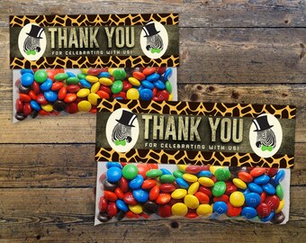 May include: Two clear cellophane bags filled with colorful M&M's candies. Each bag has a brown and yellow zebra print thank you tag with a black and white zebra wearing a top hat and bow tie. The tag says "Thank You for celebrating with us!"