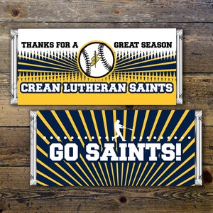 May include: Two blue and yellow baseball-themed chocolate bar wrappers. The top wrapper says "Thanks for a Great Season Crean Lutheran Saints". The bottom wrapper says "Go Saints!" with a baseball player silhouette.