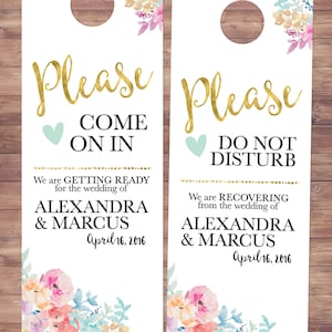 Puede incluir: Dos colgadores de puerta blancos con diseños florales y letras doradas. El colgador de la izquierda dice "Por favor, entre" y "Nos estamos preparando para la boda de Alexandra y Marcus el 16 de abril de 2016". El colgador de la derecha dice "Por favor, no molestar" y "Nos estamos recuperando de la boda de Alexandra y Marcus el 16 de abril de 2016".
