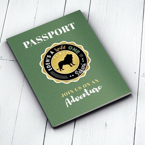 May include: Green passport-style invitation with the text "PASSPORT" in gold lettering. A gold circle with a black border and the text "EDEN'S WILD ONE SAFARI" surrounds a black silhouette of a lion. The text "JOIN US ON AN ADVENTURE" is printed in gold lettering.