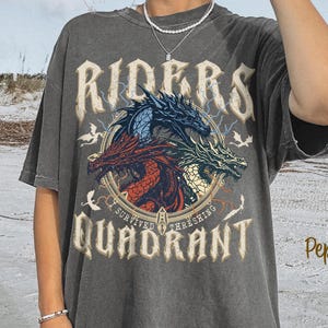 May include: Dark grey t-shirt with a graphic of three dragons in red, blue, and green, with the text "RIDERS QUADRANT". The shirt has a vintage, worn look and the word "Pepper" is printed on the bottom right.