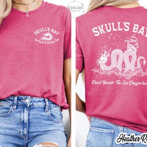 May include: Heather raspberry-colored t-shirt with white graphic text and a sea dragon design. The front of the shirt says "Skull's Bay" with a sea dragon graphic. The back of the shirt has the same text and a larger sea dragon graphic.