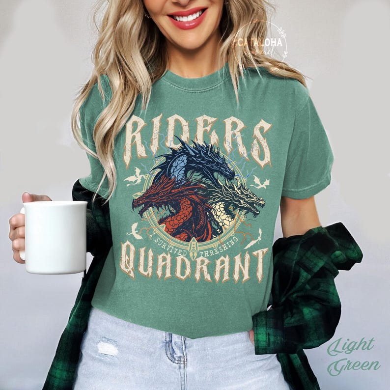 May include: Light green t-shirt with a graphic of three dragons in a circle, with the words "RIDERS QUADRANT" and "I SURVIVED THRESHING". The shirt is a solid color and has a vintage look.