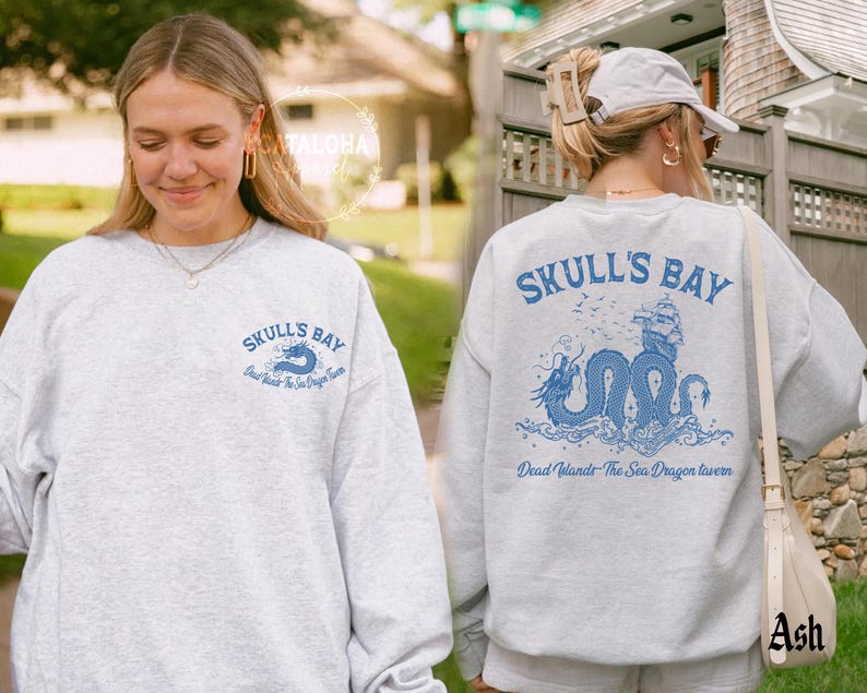 May include: Light gray sweatshirt with the text "SKULL'S BAY" in blue on the front and back. The back features a blue illustration of a sea dragon, ship, and text "Dead Islands The Sea Dragon Tavern".