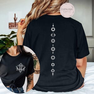 May include: Black t-shirt with a white lotus flower graphic on the front and a vertical chakra design on the back. The shirt has short sleeves and a crew neck. The brand name "CATALOHA Apparel" is printed on a circular sticker.