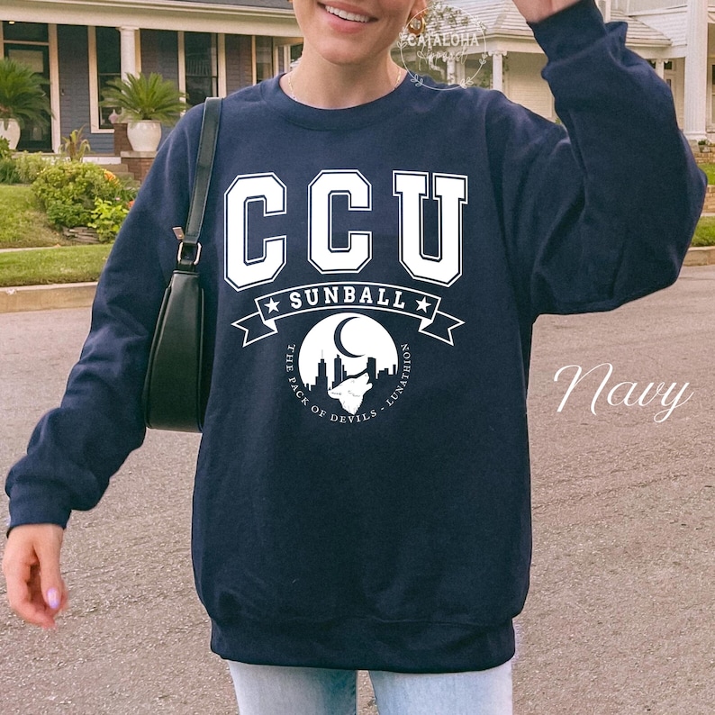 Pode incluir: Camisola azul marinho com o texto branco "CCU", "Sunball" e um gr&aacute;fico de uma lua, paisagem urbana e lobo. O texto "The Pack of Devils - Lunathion" tamb&eacute;m est&aacute; inclu&iacute;do.