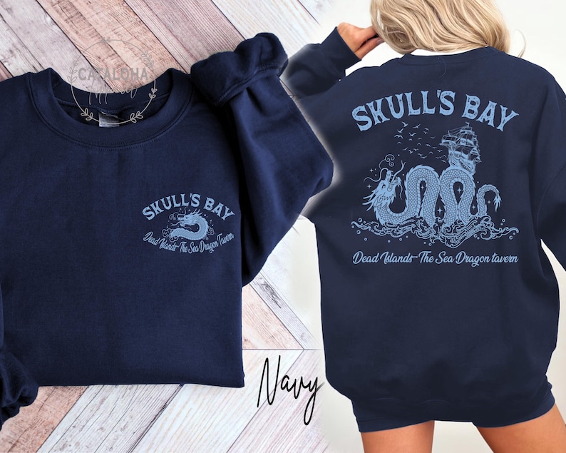 May include: Navy blue sweatshirt with "SKULL'S BAY" text and a dragon graphic on the front and back. The back design includes a ship and the text "Dead Islands - The Sea Dragon Tavern". The sweatshirt is a crew neck style.