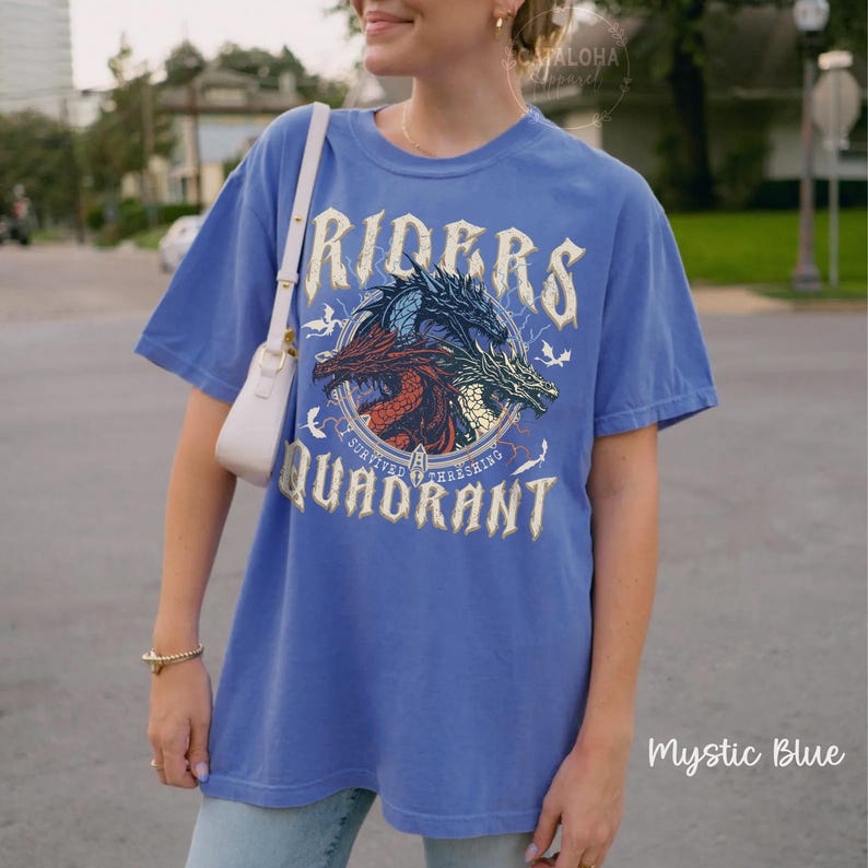 May include: Mystic blue t-shirt with a graphic of three dragons inside a circle, with the words "RIDERS" and "QUADRANT". The shirt has short sleeves and a relaxed fit. The text "Survived Threshing" is also on the shirt.