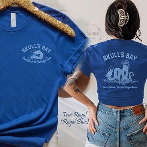 May include: Royal blue t-shirt with the text "SKULL'S BAY" and a sea dragon design. The shirt also has the text "Dead lands The Sea Dragon luver". The shirt is displayed on a gold hanger.