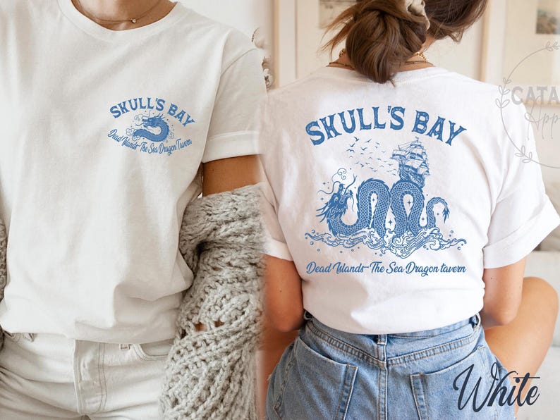 May include: White t-shirts with blue graphic designs. One shirt features "Skull's Bay" text with a dragon and the text "Dead Islands - The Sea Dragon Tavern". The other shirt has the same design on the back.