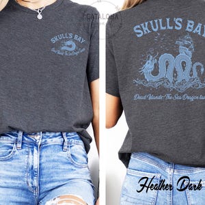 May include: Dark heather grey t-shirt with "Skull's Bay" and "Dead Wlands The Sea Dragon Tavern" printed in light blue. The back of the shirt features a light blue sea dragon design with a ship. The shirt is made of a soft material.