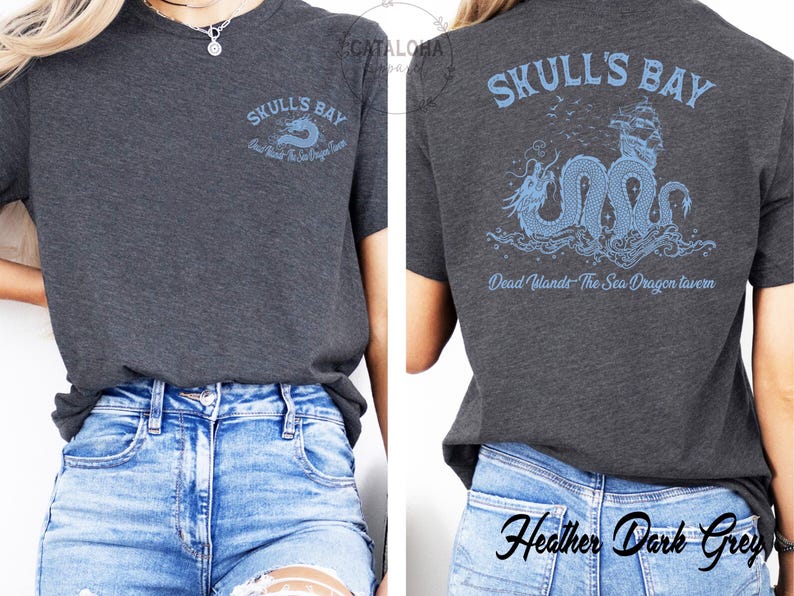 May include: Dark heather grey t-shirt with "Skull's Bay" and "Dead Wlands The Sea Dragon Tavern" printed in light blue. The back of the shirt features a light blue sea dragon design with a ship. The shirt is made of a soft material.