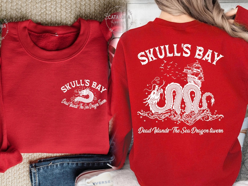 May include: Red sweatshirt with white graphic text and a dragon illustration. The text reads "SKULL'S BAY" and "Dead Islands - The Sea Dragon Tavern". The back features a ship, dragon, and text.