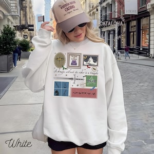 Puede incluir: Sudadera blanca con un dise&ntilde;o gr&aacute;fico que presenta ilustraciones estilo sello postal, una espada y el texto "A dragon without its rider is a tragedy". La palabra "White" est&aacute; impresa en la parte inferior.