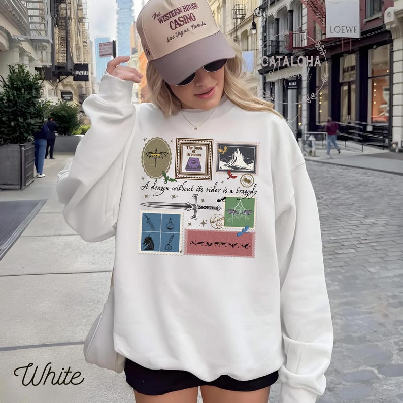 Puede incluir: Sudadera blanca con un dise&ntilde;o gr&aacute;fico que presenta ilustraciones estilo sello postal, una espada y el texto "A dragon without its rider is a tragedy". La palabra "White" est&aacute; impresa en la parte inferior.