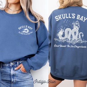 May include: Indigo blue sweatshirt with white graphic text and a dragon design. The front features "Skulls Bay" and "Dead Islands The Sea Dragon Tavern". The back displays a detailed dragon, ship, and text "Skulls Bay" and "Dead Islands The Sea Dragon Tavern".