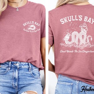 May include: Mauve short-sleeved t-shirt with "Skull's Bay" and a sea dragon graphic on the front and back. The back design includes a ship and the text "Dead Islands - The Sea Dragon Tavern".