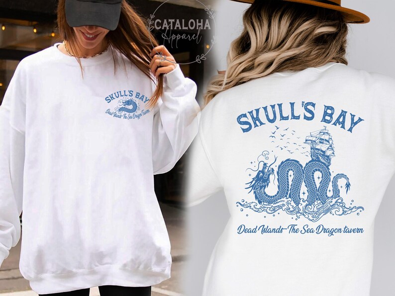 May include: White sweatshirt with blue graphic text and design. The front features "Skull's Bay" and "Dead Islands - The Sea Dragon Tavern". The back has a detailed illustration of a ship, dragon, and waves, with the same text.