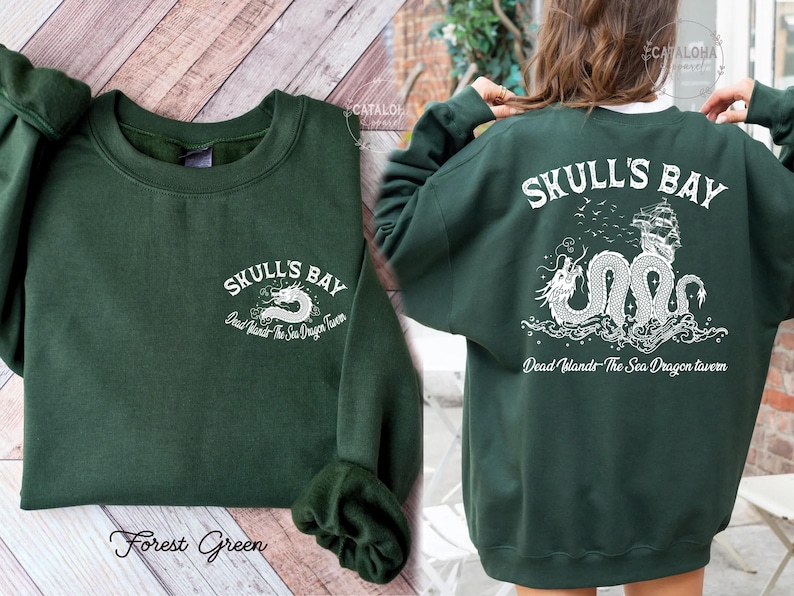 May include: Forest green sweatshirt with the text "SKULL'S BAY" and a white dragon graphic on the front and back. The back design includes a ship and the text "Dead Wands The Sea Dragon tavern".