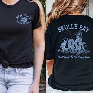 May include: Black t-shirt with a light blue graphic on the front and back. The front features the text "SKULL'S BAY" and "Dead Islands The Sea Dragon Tavern". The back has a dragon and ship design with the same text.