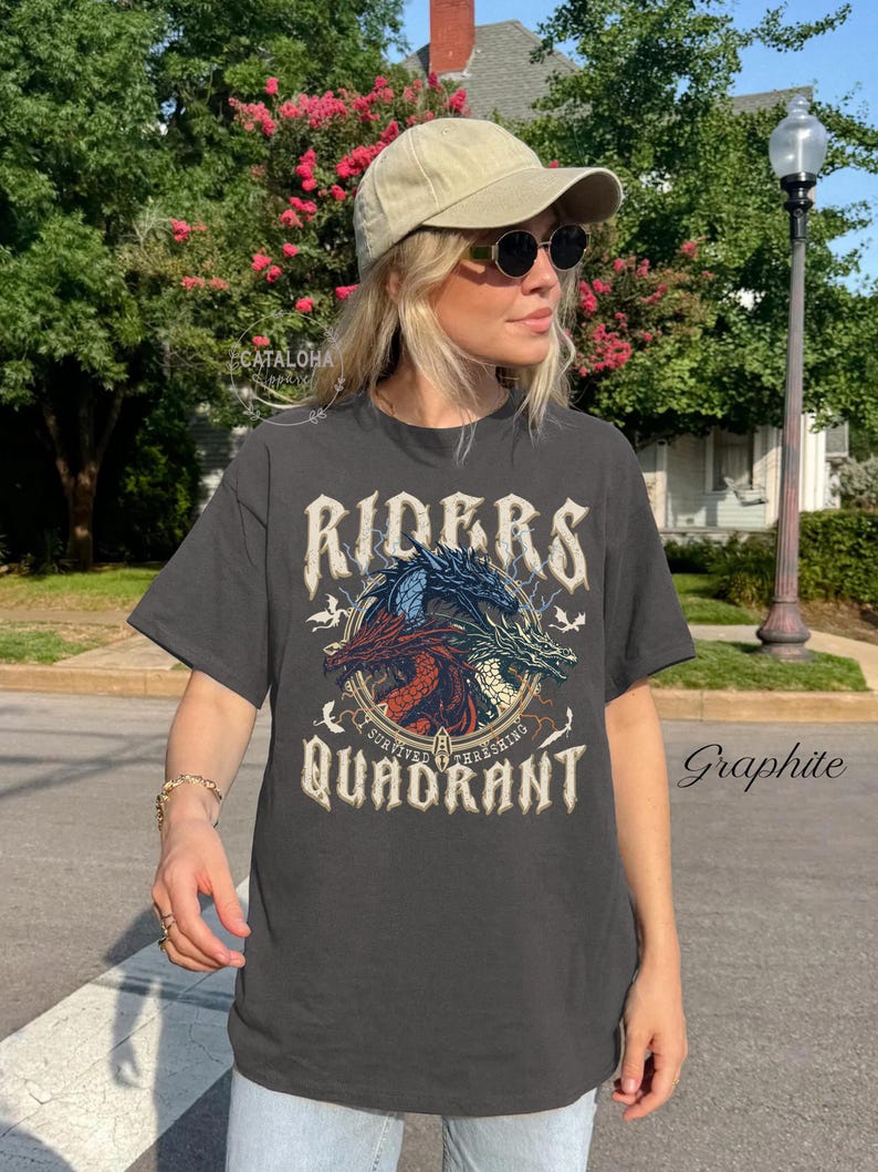 May include: Graphite-colored t-shirt featuring a dragon design with the words "Riders Quadrant". The graphic includes three dragons in red, blue, and green. The shirt is worn by a person wearing a cap and sunglasses.