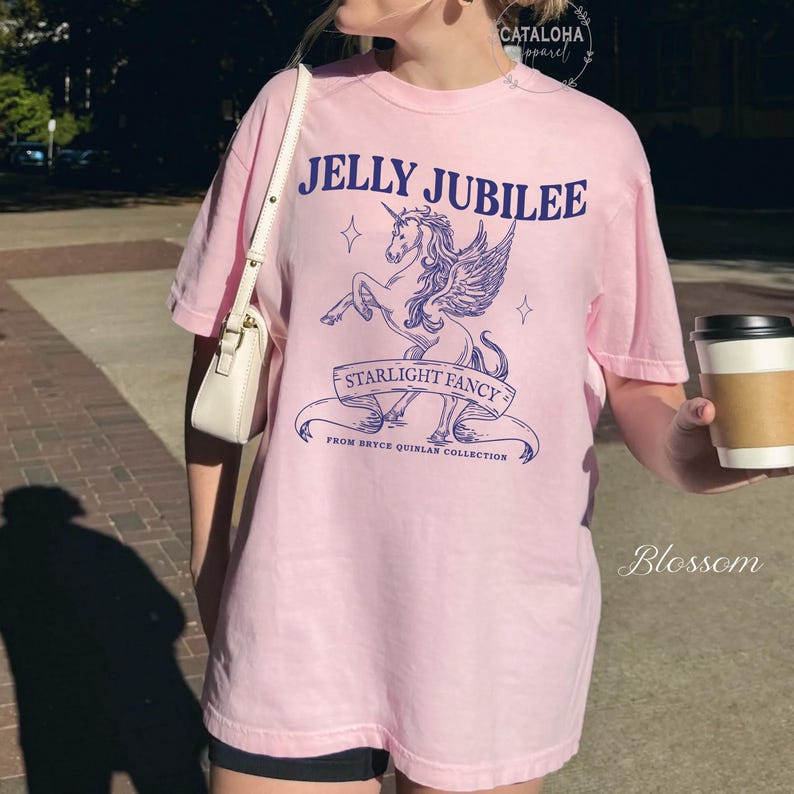 May include: A light pink t-shirt with a graphic design featuring a winged unicorn, the text "JELLY JUBILEE", and "STARLIGHT FANCY". The shirt is part of the "Bryce Quinlan Collection".