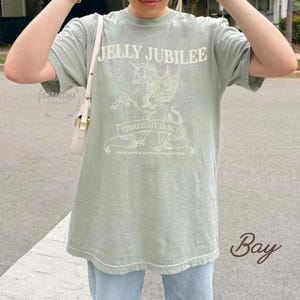 May include: Sage green t-shirt with the text "JELLY JUBILEE" above a unicorn graphic and the words "STARLIGHT FANCY" on a banner. The shirt also includes the text "FROM BRYCE QUINLAR COLLECTION".