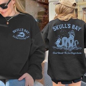 May include: Black sweatshirt with "SKULL'S BAY" text and a blue dragon graphic. The text "Dead Islands The Sea Dragon Tavern" is also printed on the sweatshirt. The design is on the front and back of the sweatshirt.