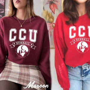 Pode incluir: Camisolas bord&ocirc; e vermelhas. Cada camisola apresenta o texto "CCU" em letras brancas, com "SUNBALL" e um gr&aacute;fico de um lobo uivando para a lua. O texto "THE PACK OF DEVILS - LUNATICS" tamb&eacute;m est&aacute; inclu&iacute;do.