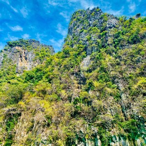 May include: A view of a large, rocky island with lush green vegetation. The island is surrounded by clear, turquoise water.