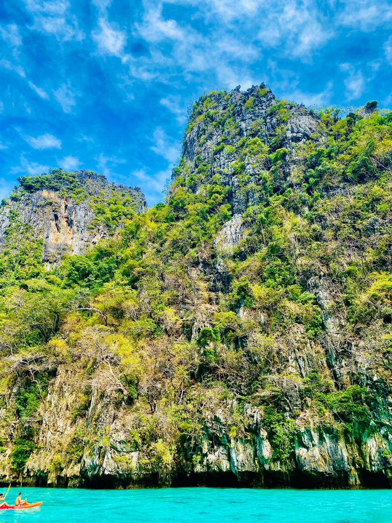May include: A view of a large, rocky island with lush green vegetation. The island is surrounded by clear, turquoise water.