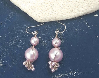 May include: A pair of pink pearl earrings with silver wire wrapped around the pearls. The earrings have a cluster of smaller pearls dangling from the bottom.