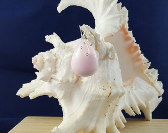 May include: A pink teardrop-shaped pendant earring with a silver wire design, displayed on a white seashell.