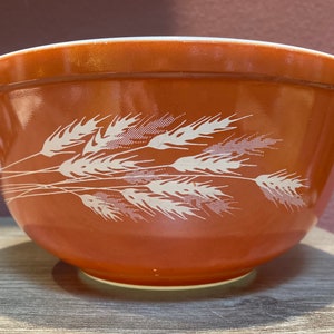 May include: A large, orange-brown mixing bowl with a white wheat design. The bowl is made of glass and has a smooth, glossy finish.